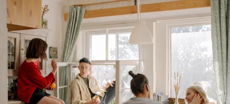 Four young roommates relaxing together in a bright shared apartment kitchen
