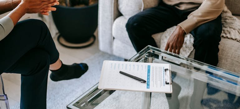 A clipboard with a printed form on a glass table between two people talking