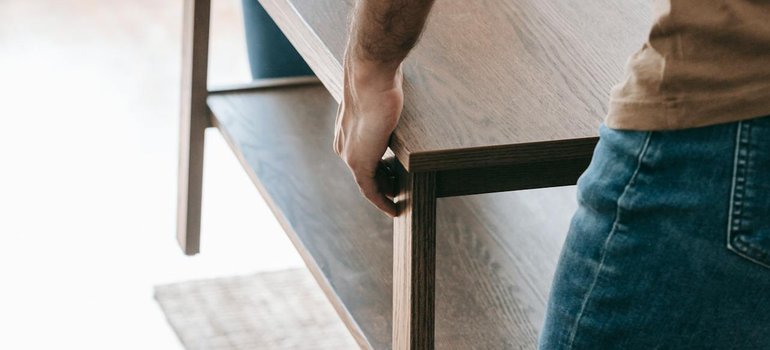 A mover carrying a wooden table, showing why buildings want a certificate of insurance for movers