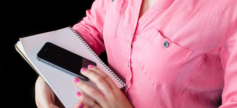 A woman holding a notebook and phone while planning a move