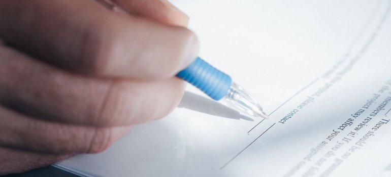 A hand signing a printed lease agreement with a blue pen