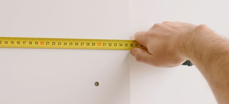 A hand pulling a tape measure across a white wall to check dimensions