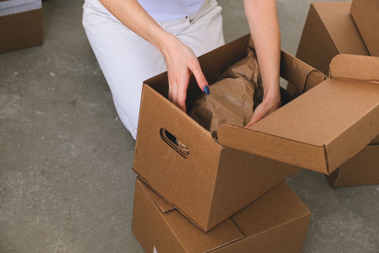 A person packing items into cardboard moving boxes before loading a truck