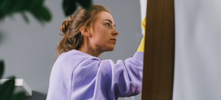A woman in yellow rubber gloves wiping down a surface while cleaning an apartment